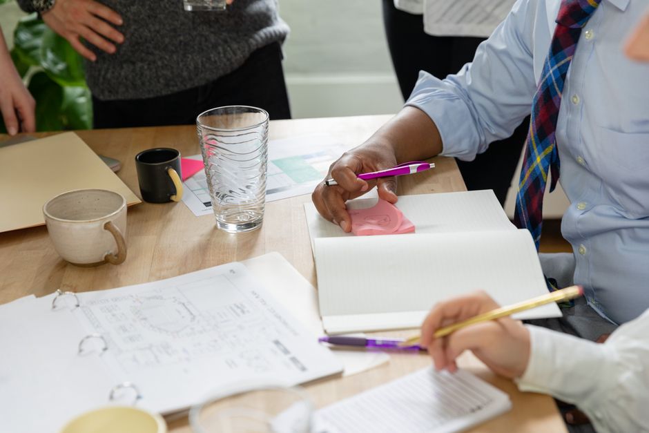 Business meeting with individuals taking notes on notebooks and discussing ideas at a wooden table.